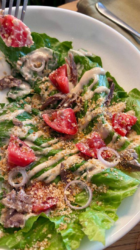 Салат с листьями романо, помидорами и кольцами лука, приправленный соусом и посыпанный сыром; сервировка на белой тарелке.