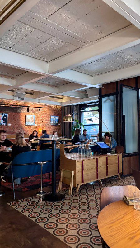 Интерьер ресторана с уютными диванами, столиками и дизайнерскими элементами — вид на зал и посетителей за трапезой.