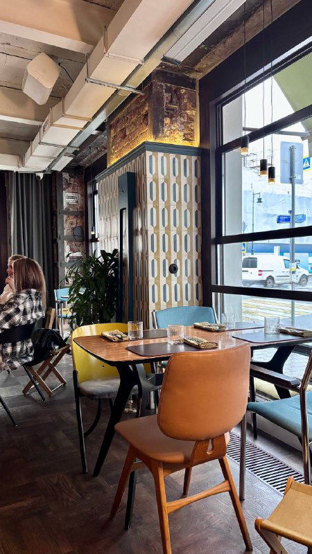 Зона в ресторане с большими окнами, столиками и стульями — дневное освещение и элементы декора на стенах.
