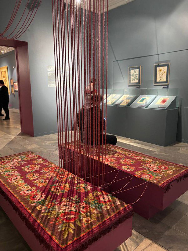 Выставочный зал с двухслойными коврами и подвесными элементами: на переднем плане декоративные ковры и нитяные инсталляции в музее.