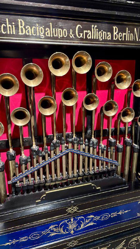 Ряд медных рожков и механических трубок автоматической музыкальной машины на красном бархатном фоне в витрине музея «Собрание».