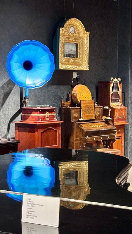 Экспозиция с различными музыкальными инструментами и синим рупором рядом с роялем — сочетание антиквариата и интерьерных деталей зала.