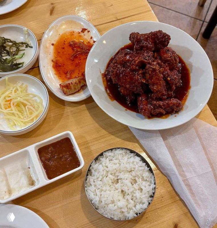 Тарелка с тушёным мясом в тёмном соусе, рядом миска белого риса и несколько маленьких закусок — домашняя и сытная подача порции.