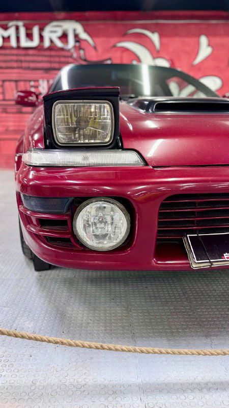 Красный передний бампер и крупный головной фонарь ретро-автомобиля в музее, фокус на деталях передней части и хромированных элементах.