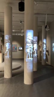 Зал с колоннами и множественными вертикальными проекциями движущихся фигур танцоров — современная инсталляция части экспозиции.