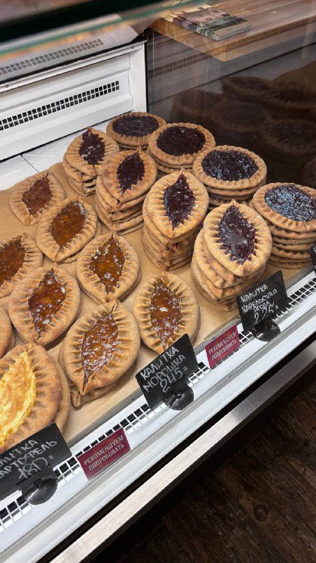 Острые кадры витрины с разными калитками и пирогами в прилавке пекарни; видны формы изделий и ценники у каждой серии печений.