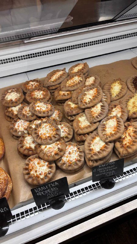 Холодная витрина с маленькими калитками разной начинки: творог, картошка и другие варианты аккуратно уложены в ряд на подносе.