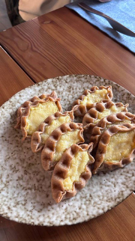 Порция свежих калиток на тарелке в кафе: рифлёные края теста и золотистая начинка, готовое подача в простом уютном интерьере.