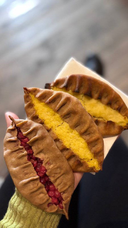 Разрезанные калитки с разными начинками — тёмная ягодная и светлая тыквенно-картофельная; руки держат кусочки на фоне деревянного стола.