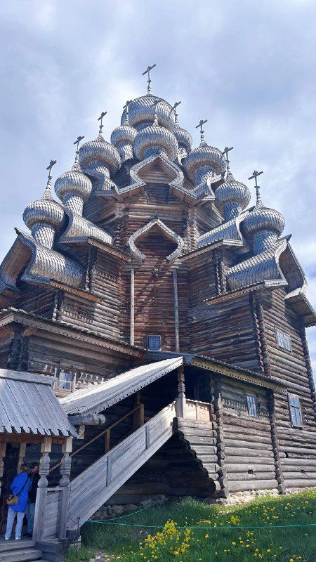 Многокупольный деревянный храм на острове Кижи — резные доминанты и деревянная архитектура под ясным небом, туристы у основания.