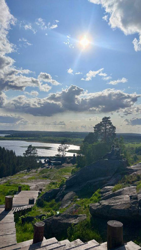 Панорамный вид с вершины: река, лес и поля внизу, солнце и облака, скамейки и тропа на смотровой площадке — вид с горы Паасонвуори.