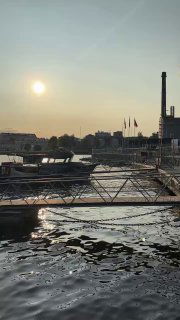 Гаванская сцена на закате: причалы, лодки и промышленные сооружения на фоне неяркого солнца, тихий морской пейзаж в порту.