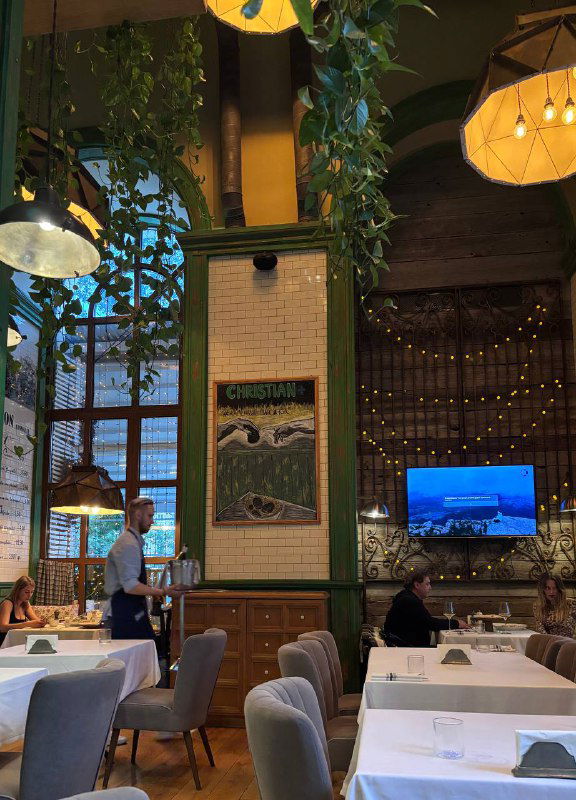 Интерьер ресторана Christian: высокий зал с зелёными колоннами, столами и декоративными элементами, вид на посадочные места и атмосферу заведения в Москве