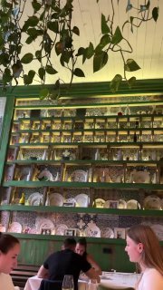 Высокая стеллажная полка с посудой и растениями, посетители у столов внизу — витрина интерьерных решений ресторана Christian в Москве на Кутузовском проспекте