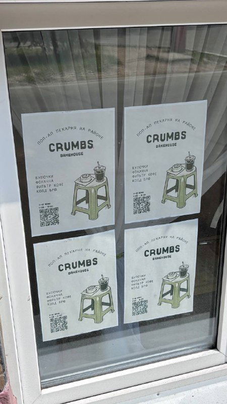 Афиши и листовки Crumbs в окне с логотипом, информацией о поп‑апах и QR‑кодами — вывеска отражает формат выездных продаж и сменных локаций