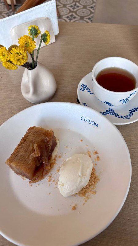 Десертный кадр: яблочный татен с шариком мороженого на тарелке с логотипом Claudia и чашка чая, минималистичный столовый декор.