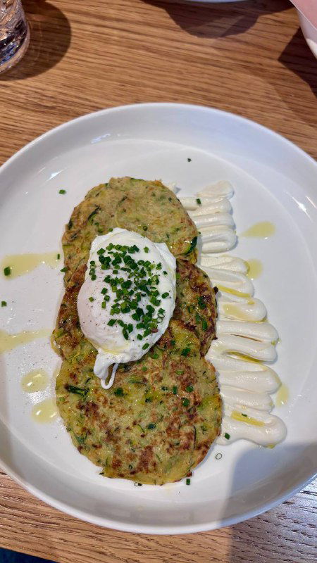 Подача оладий или котлет с соусом и зеленью на белой тарелке — пример кухни Rebellion, акцент на простых домашне-урбанистических блюдах.