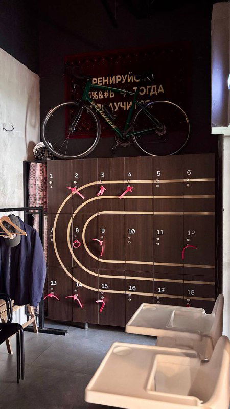 Декоративная экспозиция с велосипедом и трассой на стене у входа в кафе; мерч-стеллажи и велосипед как часть фирменного стиля Rebellion.