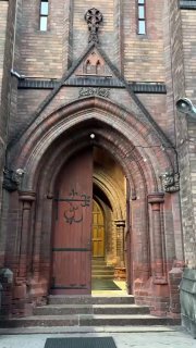 Главный вход в английскую церковь Святого Андрея: массивные деревянные двери с коваными элементами и арочный портал, открыт вечерний проход внутрь.