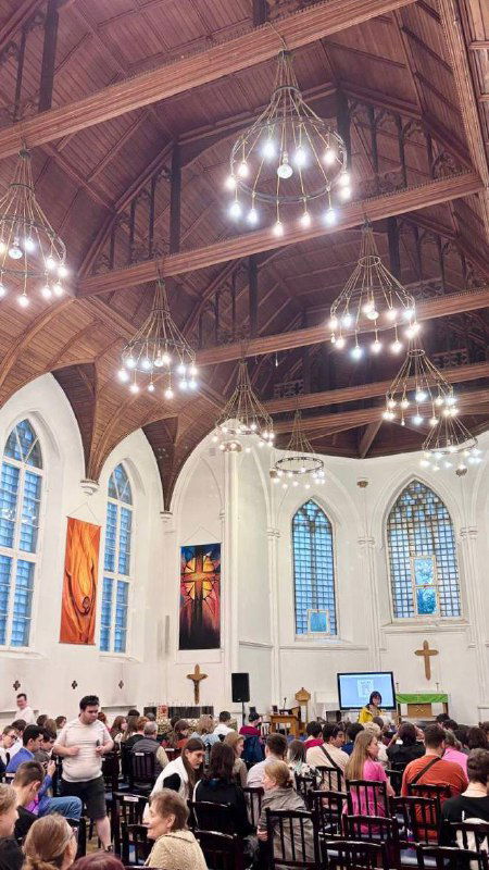 Внутренний простор англиканской церкви Святого Андрея во время службы: расставленные скамьи, деревянный сводчатый потолок и подвесные люстры.