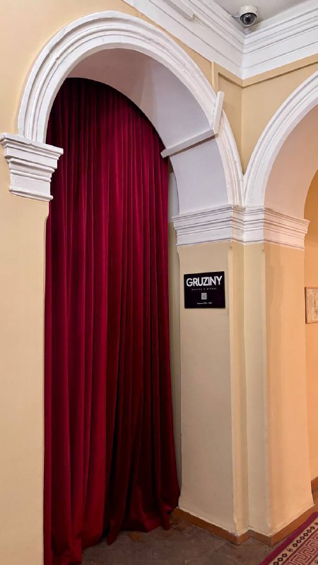 Арочный проём с высоким лепным потолком и тяжёлыми бархатными занавесями глубокого бордового цвета в одном из камерных залов усадьбы.