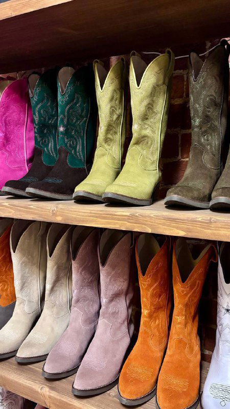 Полка с разнообразными замшевыми казаками — ряд ярких сапог ковбойской формы, текстура и насыщенные цвета в бутике усадьбы.