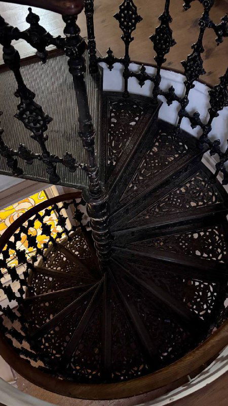 Вид сверху на винтовую лестницу: закрученные ступени чёрного чугуна, узорная кладка ступеней и симметричный центр лестничного пролёта в интерьере усадьбы.