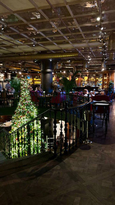 Интерьер ресторана: широкая винтовая лестница, украшенная рождественской ёлкой и праздничной иллюминацией, вид на зал и ограждение.