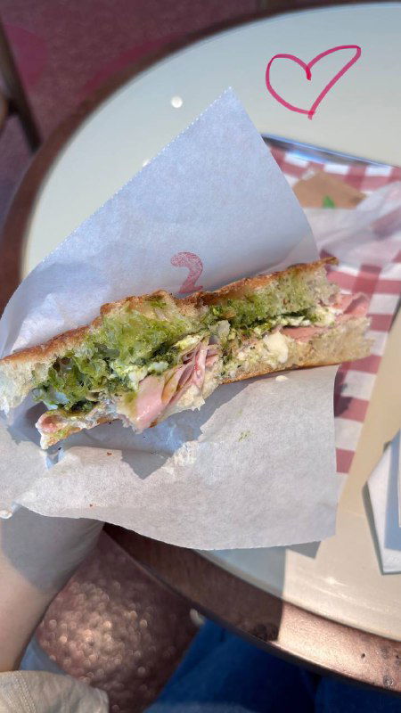 Фокачча с зелёным песто и слоями сыра, разрезанный кусок на белой бумаге, видно зелёный песто, страчателла и начинки на фоне столика.