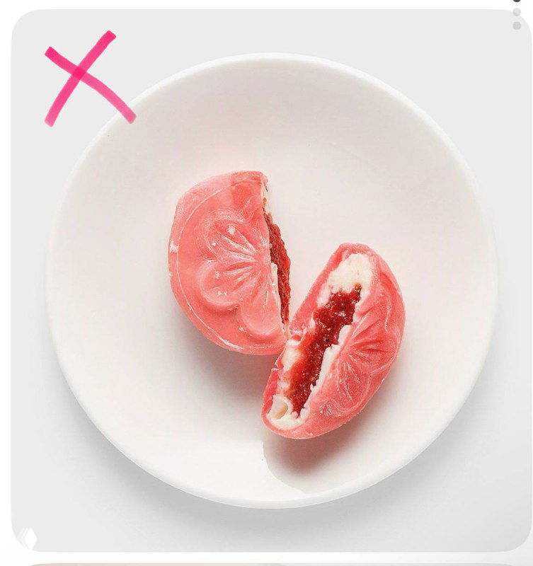 Розовый моти-кейк разрезан пополам на белой тарелке: видна клубничная начинка и розовая оболочка, стильная продуктовая подача.