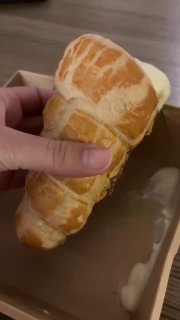 Рука держит большую слоёную бриошь или булочку с явными слоями теста, вид сбоку, коричневая корочка и мягкий мякиш внутри.