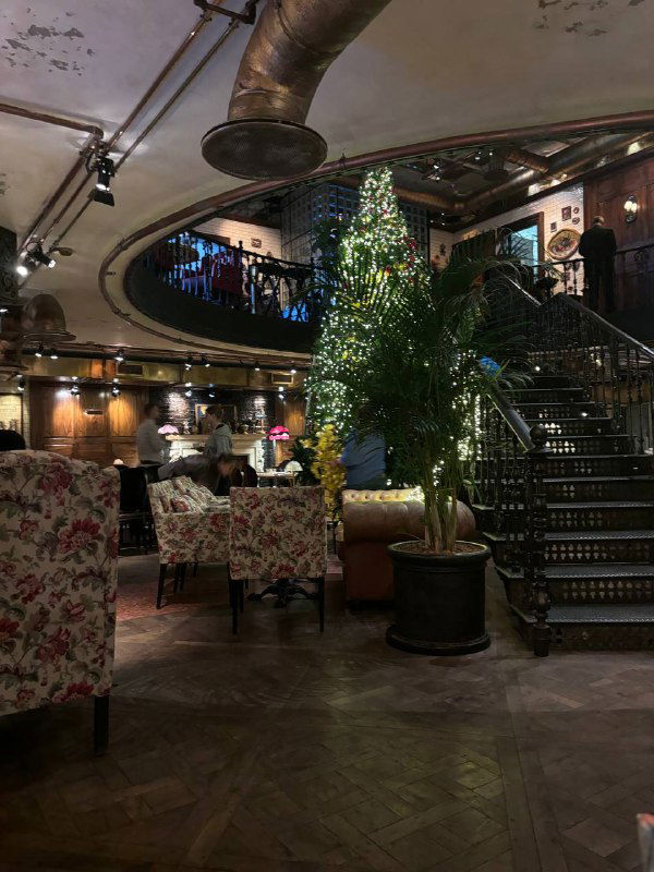 Просторный зал ресторана с витой лестницей, цветочными креслами и тёплой атмосферой; вид на верхний ярус и декоративные элементы.