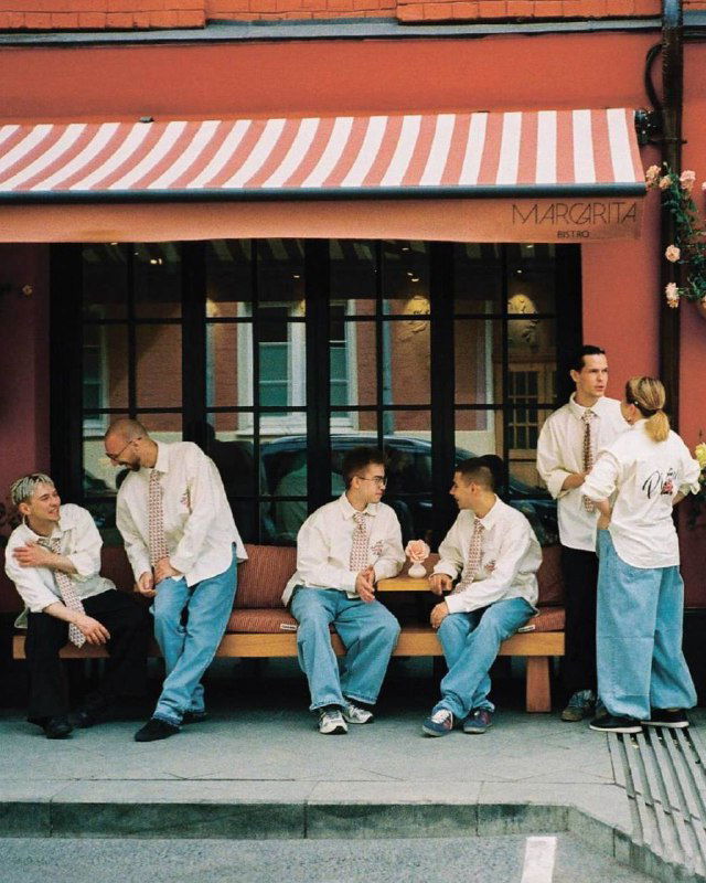 Группа официантов в фирменной униформе сидит у фасада Margarita Bistro: форма отражает концепцию коллаборации и общую эстетическую подачу заведения.