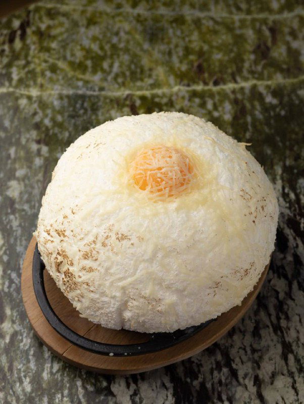 Десерт или хлебная подача: круглый тёплый шар с легкой посыпкой, сервированный на тарелке с деревянной подставкой — эстетичная подача блюда.