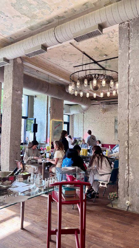 Интерьер бистро Метеорит: высокий потолок, кирпичные колонны, гости за столиками и большая люстра над залом ресторана.