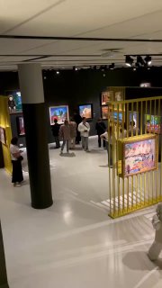 Интерьер выставочного зала: посетители рассматривают картины в обрамлении металлических перегородок и яркого освещения, общий ракурс зала.