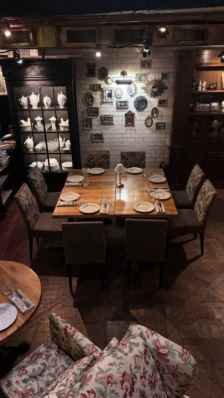 Набор столиков и полки с сервированными предметами: узорчатые кресла и тёплая деревянная отделка интерьера ресторана.