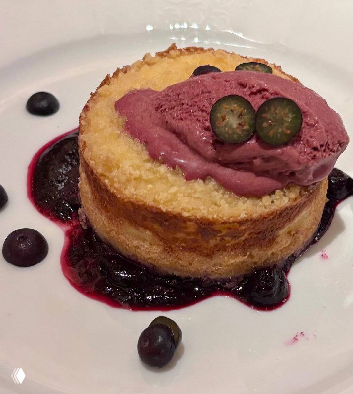 Царская ватрушка с мороженым и черничным соусом на белой тарелке: творожный пирог, ягодная подача и сливочный шар мороженого сверху.