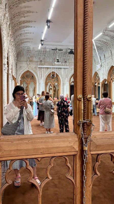 Посетители отражаются в зеркале дворцового интерьера: люди в зале осматривают орнаментальную лепнину и декоративные двери усадьбы