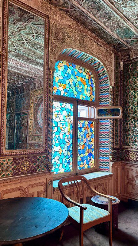Витражное окно и фигурная расписная отделка арабского зала усадьбы: стол и деревянное кресло на фоне цветного стекла и мозаики