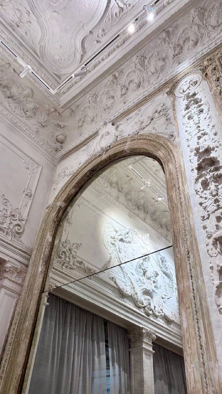 Отражение высокого арочного зеркала и лепных украшений на стене в одном из салонов усадьбы с богатой декоративной отделкой