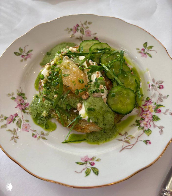 Порция салата или закуски с ломтиками огурца, соусом и зеленью на тонком фарфоровом блюде с цветочным орнаментом.