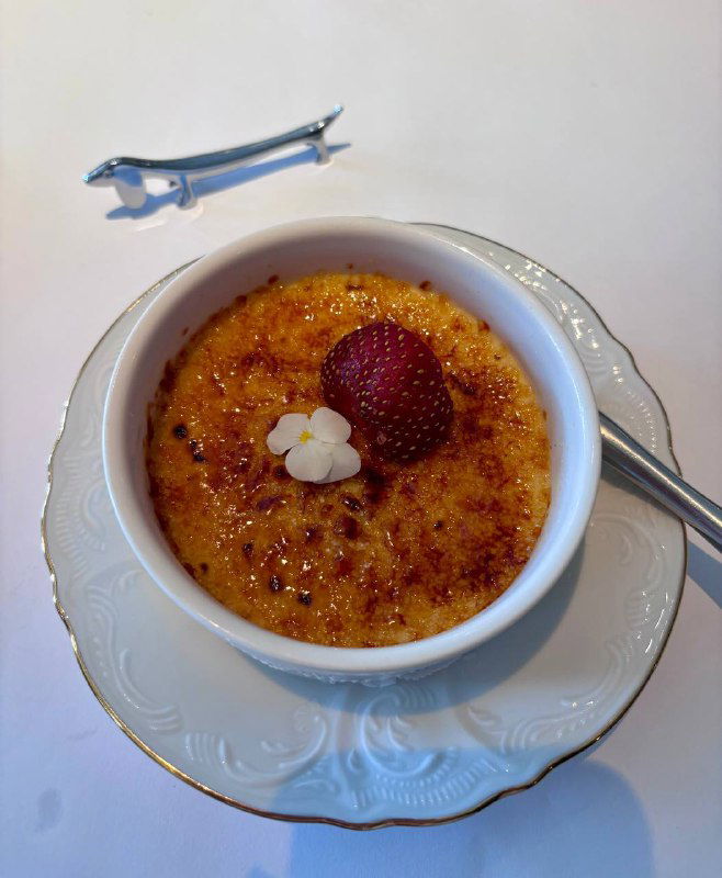 Крем‑брюле в керамической формочке с карамелизированной корочкой и ягодой сверху, сервировано на белой тарелке.