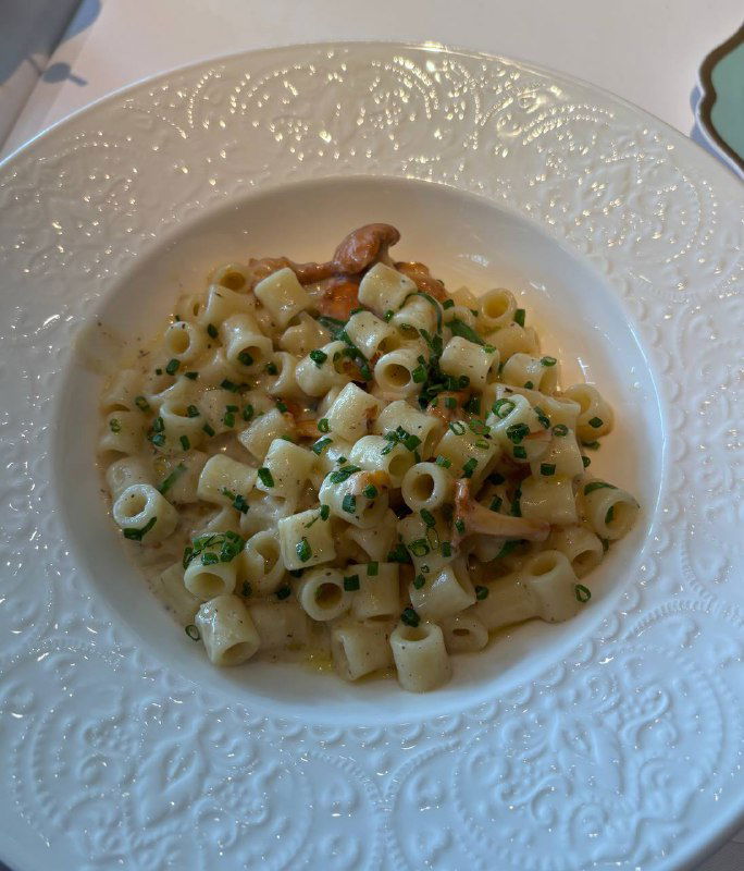 Паста с лисичками в кремовом соусе, сервированная в белой текстурной тарелке — крупный план пасты и грибов.