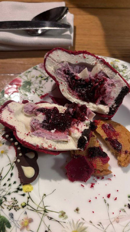 Десерт, разрезанный на части: сливочная начинка и ягодный соус на декоративной тарелке, остатки украшений и текстуры крема.