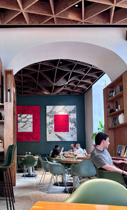 Глубокий вид на зал кафе с резным деревянным потолком, картинами на стене и сидящими посетителями — уютная атмосфера для завтрака.