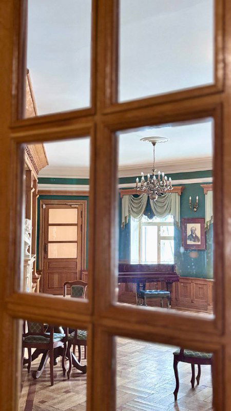 Интерьер с видом через стеклянные двери на соседний зал: деревянная мебель, люстра и мягкие тона помещения, классический ретро‑интерьер.