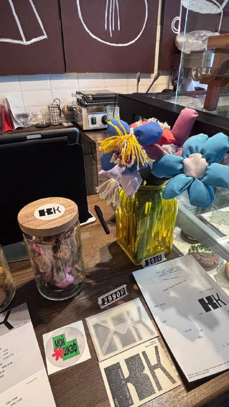 Витрина и столик с декоративными тканевыми цветами, баночками и печатными материалами — детали оформления и атрибутика мастер‑класса.