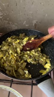 Обжаренная стручковая фасоль с кусочками яйца в сковороде, деревянная ложка перемешивает смесь — видно этап готовки блюда.