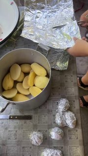 Крупный план картошки, уложенной в кастрюлю и завернутой в фольгу, а рядом несколько фольгированных «картофелин» готовы лечь в угли.